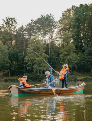 Opa zit met twee kleinkinderen in een roeibootje, kinderen zijn aan het vissen