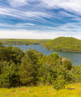 Uitzicht over een meer met groene heuvels en bos bij een vakantiepark met glamping accommodaties.