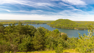 Uitzicht over een meer met groene heuvels en bos bij een vakantiepark met glamping accommodaties.
