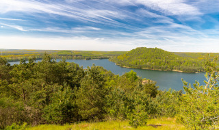 Vista panorámica de un lago rodeado de colinas y bosque en un parque vacacional con glamping.