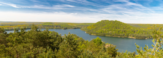 Uitzicht over een meer met groene heuvels en bos bij een vakantiepark met glamping accommodaties.
