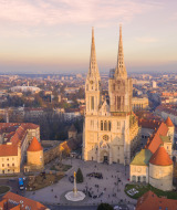 Vista aérea de una majestuosa catedral de dos torres en el centro de la ciudad, rodeada de edificios al atardecer.