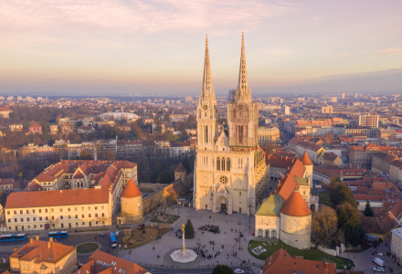 Luchtfoto van een grote kathedraal met twee torens in het stadscentrum, omringd door gebouwen bij zonsondergang.