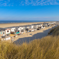 Vista di casette sulla spiaggia e dune sabbiose in un parco vacanze con alloggi glamping sul mare.