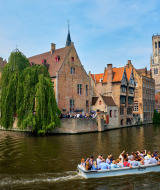 Barco turístico navega por el canal junto a edificios históricos y el campanario de Brujas, cerca de Jabbeke.