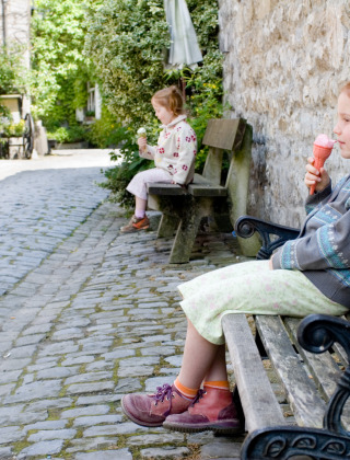Dos niñas disfrutan de un helado sentadas en bancos en una calle adoquinada de La Roche-en-Ardenne, Bélgica.