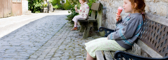 Due ragazze mangiano il gelato sedute su una panchina in una strada acciottolata a La Roche-en-Ardenne, Belgio.
