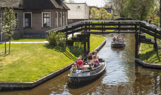 Zwei Boote fahren unter einer Holzbrücke vorbei an Häusern in Giethoorn, Overijssel, Niederlande