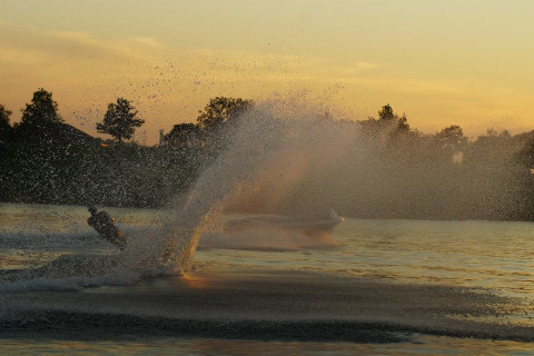 Een waterskiër maakt een hoge spettergolf op een meer bij zonsondergang in Camping de Boomgaard.