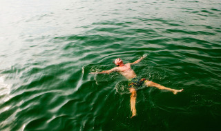 Un homme flotte tranquillement sur le dos dans l’eau verte d’un parc de vacances avec glamping.