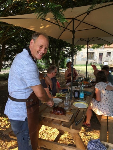 Man snijdt vlees aan een picknicktafel tijdens een zomerse barbecue in Camping la Cour d'Enchère, Frankrijk.