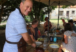 Man snijdt vlees aan een picknicktafel tijdens een zomerse barbecue in Camping la Cour d'Enchère, Frankrijk.