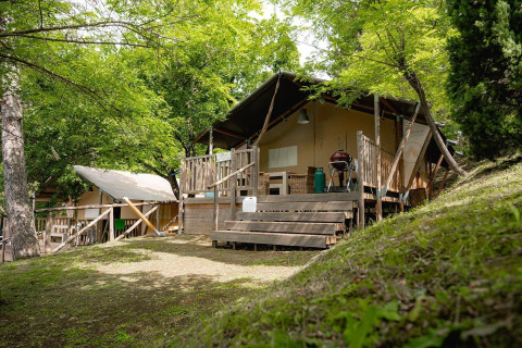 Tienda safari Villatent Wood en Camping Colleverde, Italia, rodeada de árboles y vegetación verde.