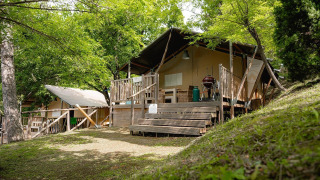 Tienda safari Villatent Wood en Camping Colleverde, Italia, rodeada de árboles y vegetación verde.