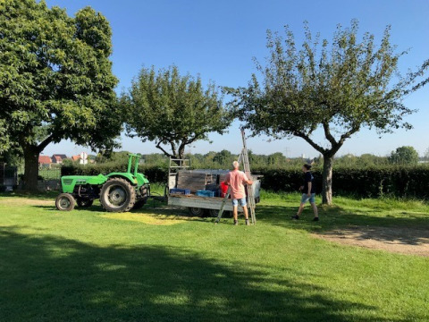 Twee mannen met landbouwmachine en kar onder bomen in vakantiepark Camping Catsop, Limburg, Nederland.