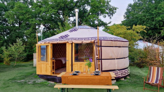 Een Mongoolse yurt met houten deur, gedekte tafel en stoel in het groen bij Zomerlicht, Nederland.