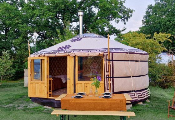 Een Mongoolse yurt met houten deur, gedekte tafel en stoel in het groen bij Zomerlicht, Nederland.