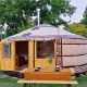 En traditionel mongolsk yurt med trædør, dækket bord og en stol, omgivet af grøn natur i Nederlandene.