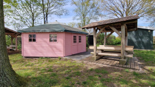 Roze tiny house genaamd Writers hut bij Zomerlicht, Nederland, met houten bank onder een afdak.