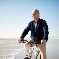 Hombre mayor monta en bicicleta por la playa en un parque vacacional con opciones de glamping al sol.