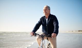 Hombre mayor monta en bicicleta por la playa en un parque vacacional con opciones de glamping al sol.
