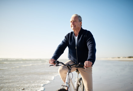 Hombre mayor monta en bicicleta por la playa en un parque vacacional con opciones de glamping al sol.