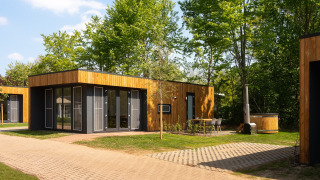 Modern wooden lodges with large windows, outdoor seating, and trees in the background at a lodge.