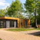 Moderne træhytter med store vinduer ved et lodge, omgivet af grønne træer og udendørs siddeplads.