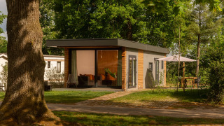 Modern tiny cabin at Holiday Park Mölke in the Netherlands, surrounded by trees and outdoor seating area.