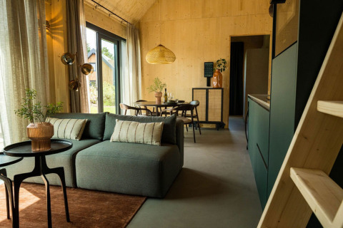 Interior moderno de lodge con sofá verde y comedor en Unbrick One | Sauna, Brinckerduyn, Países Bajos.