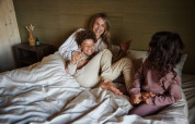 Una familia se relaja sobre una cama en una cabaña, sonriente y disfrutando juntos de un momento acogedor.