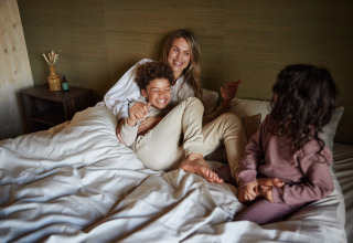 Una familia se relaja sobre una cama en una cabaña, sonriente y disfrutando juntos de un momento acogedor.
