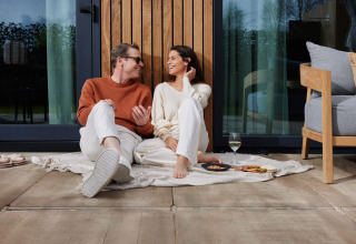 To personer sidder på et tæppe udenfor Unbrick One | Sauna ved Brinckerduyn, Holland, og nyder vin.