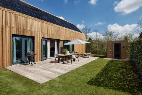 Moderna cabaña de madera con paneles solares, terraza, barbacoa y sauna en Brinckerduyn, Países Bajos, en un día soleado.