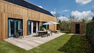 Moderna cabaña de madera con paneles solares, terraza, barbacoa y sauna en Brinckerduyn, Países Bajos, en un día soleado.