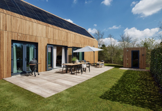 Moderne houten lodge met zonnepanelen, terras, barbecue en sauna bij Brinckerduyn, Nederland, op een zonnige dag.