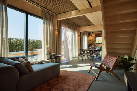 Sala de estar moderna de casa de campo con grandes ventanales, sofá, silla y comedor en Unbrick One | Sauna y Piscina en Brinckerduyn, Países Bajos.