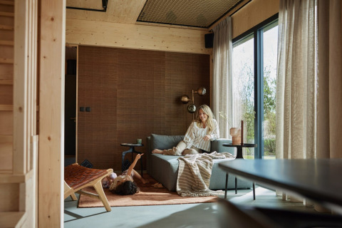 En moderne stue i Unbrick One-lodgen i Brinckerduyn, Holland, med en kvinde på sofaen og et barn på gulvet.
