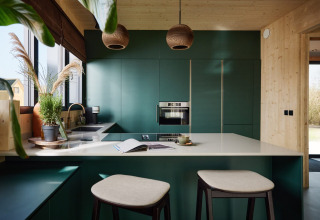 Moderne køkken med grønne skabe, træpaneler, store vinduer og barstole i Unbrick One-lodge i Holland.