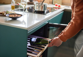 A person stores a wine bottle in a wine cooler in a modern kitchen at Brinckerduyn lodge, Netherlands.