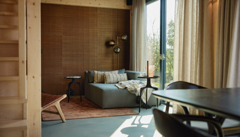 Sala moderna con sofá, pared de madera y grandes ventanales en Unbrick One Lodge, Brinckerduyn, Países Bajos.