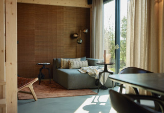 Sala moderna con sofá, pared de madera y grandes ventanales en Unbrick One Lodge, Brinckerduyn, Países Bajos.