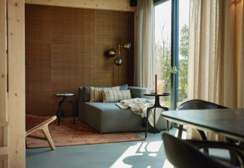 Modernes Wohnzimmer mit Sofa, Holzwand und großen Fenstern im Unbrick One Lodge, Brinckerduyn, Niederlande.