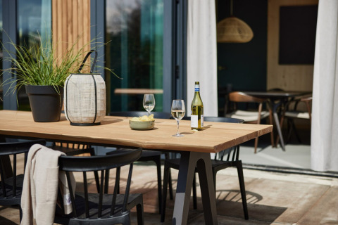 Mesa de comedor exterior con vino, dos copas, planta y farol en Unbrick One | Sauna and Pool, Brinckerduyn, Países Bajos.