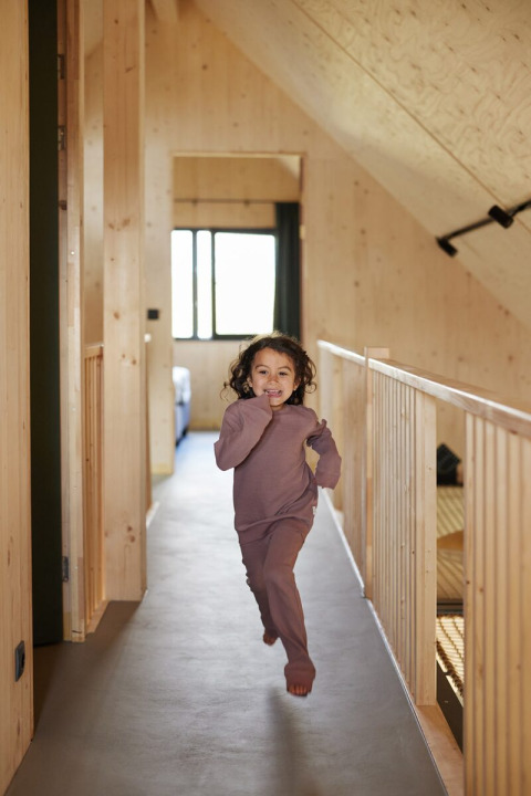 Un bambino corre a piedi nudi in un corridoio di legno a Unbrick One | Sauna and Pool a Brinckerduyn, Paesi Bassi.