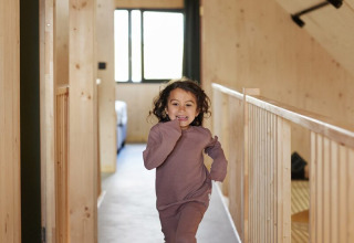 Een kind loopt blootsvoets door een houten gang in Unbrick One | Sauna and Pool in Brinckerduyn, Nederland.