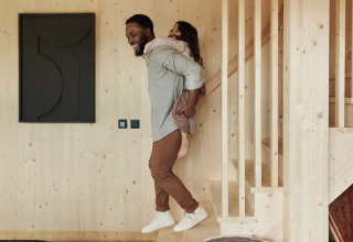 Een man draagt een kind op zijn rug in een houten lodge bij Unbrick One | Sauna and Pool in Brinckerduyn, Nederland.