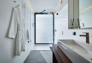 Baño moderno y luminoso con bata, lavabo y ducha en Unbrick One | Sauna and Pool, Brinckerduyn, Países Bajos.