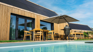 Moderne houten lodge met terras, zwembad, parasol en barbecue bij Brinckerduyn in Nederland, zonnige dag.