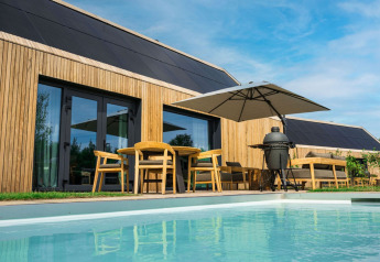 Lodge moderno de madera con terraza, piscina, sombrilla y barbacoa en Brinckerduyn, Países Bajos, día soleado.